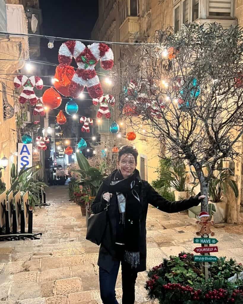 Frau steht abends in einer festlich geschmückten Straße in Malta mit Lichtern und Weihnachtsdekoration – Leben und Arbeiten im Ausland mit Online-Business.