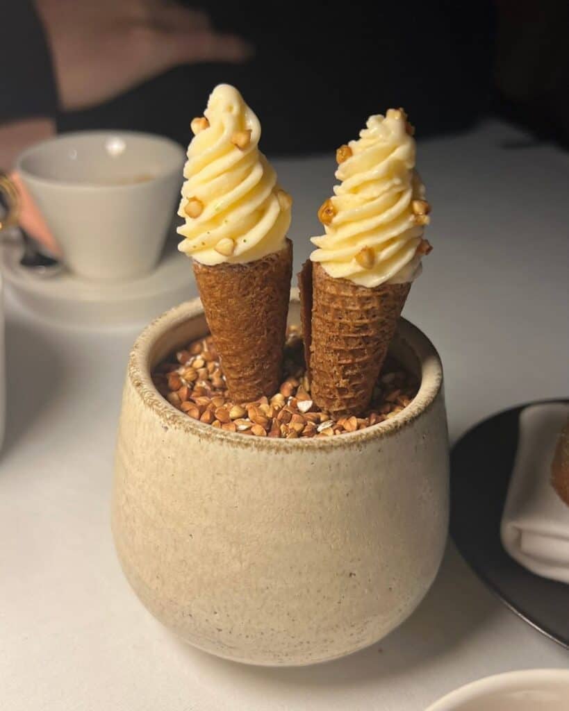 Zwei kleine Eistüten mit cremigem Dessert in einem Gefäß auf einem Tisch – Genussmoment und Lebensqualität beim Leben und Arbeiten im Ausland.