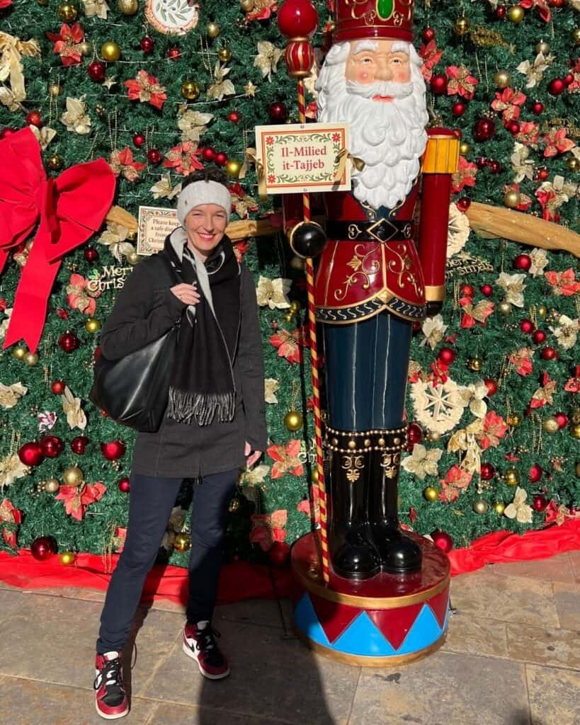 Frau steht lächelnd vor einer weihnachtlich geschmückten Kulisse mit großer Nussknacker-Figur in Malta – Leben und Arbeiten im Ausland zur Weihnachtszeit.