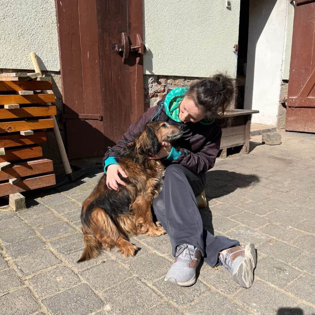 Frau sitzt im Hof und streichelt liebevoll ihren Hund – authentischer Einblick in Persönlichkeit und Werte.