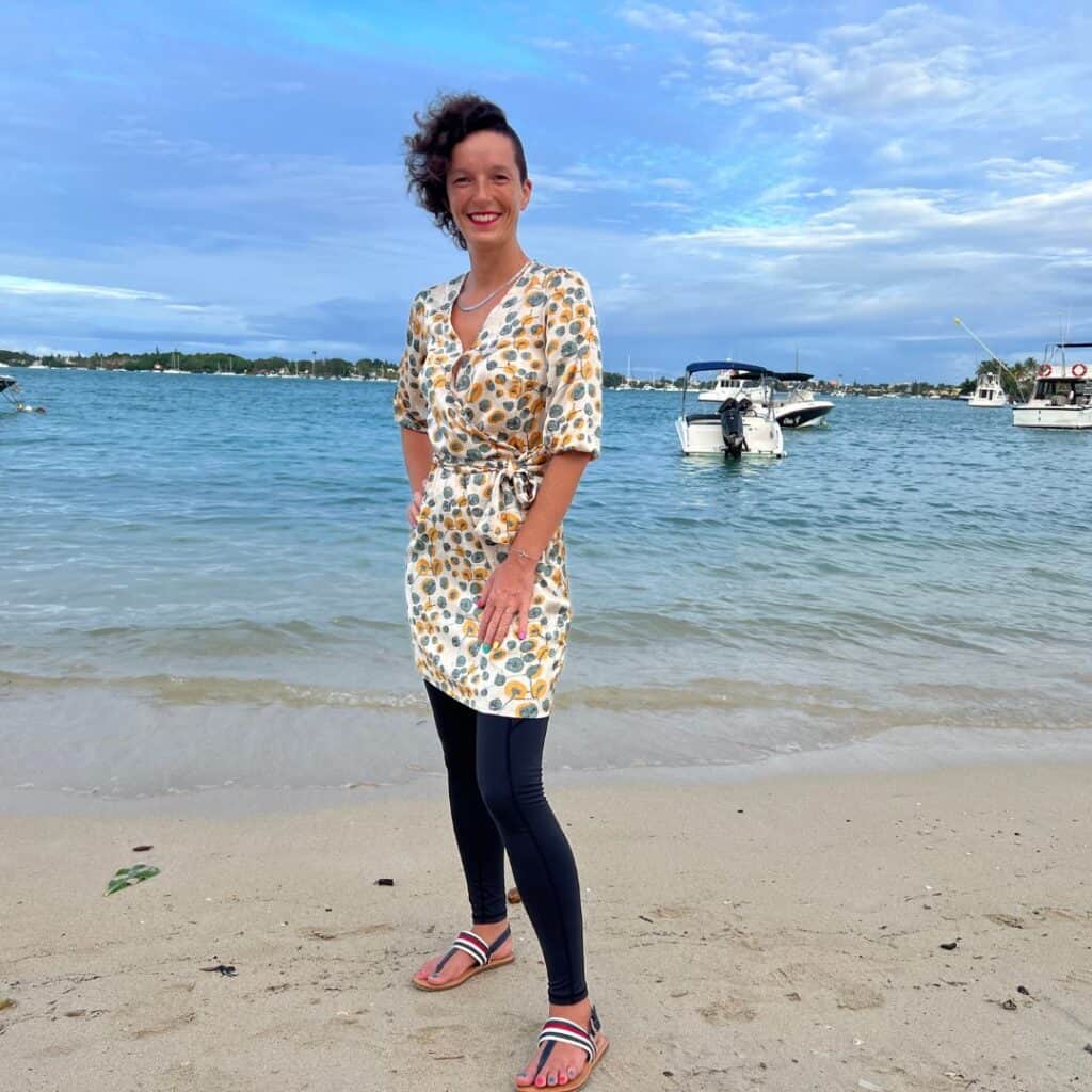 Frau steht lächelnd am Strand mit Meer im Hintergrund – Technik-Begleiterin für Onlinekurse, Newsletter und Onlinebusiness.