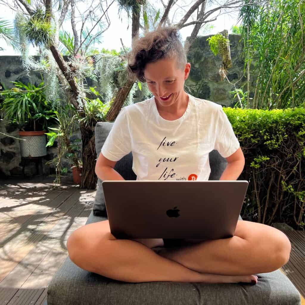 Frau sitzt entspannt im Schneidersitz im Freien und arbeitet konzentriert am Laptop – Technik-Begleiterin für Onlinekurse und Onlinebusiness.